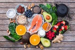 Overhead picture of various foods like avocados, salmon, spinach and oranges.