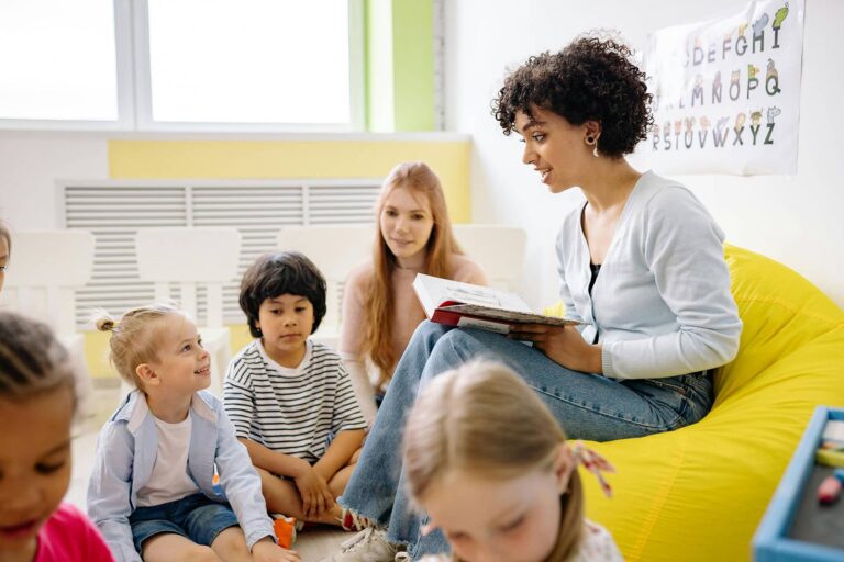 Woman sitting in bean bag chair reading book to kids.