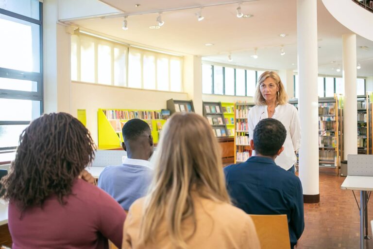 Woman presenting to group seated in library.