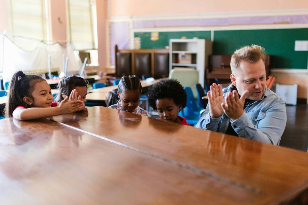 Adult with children clapping at a table in a classroom