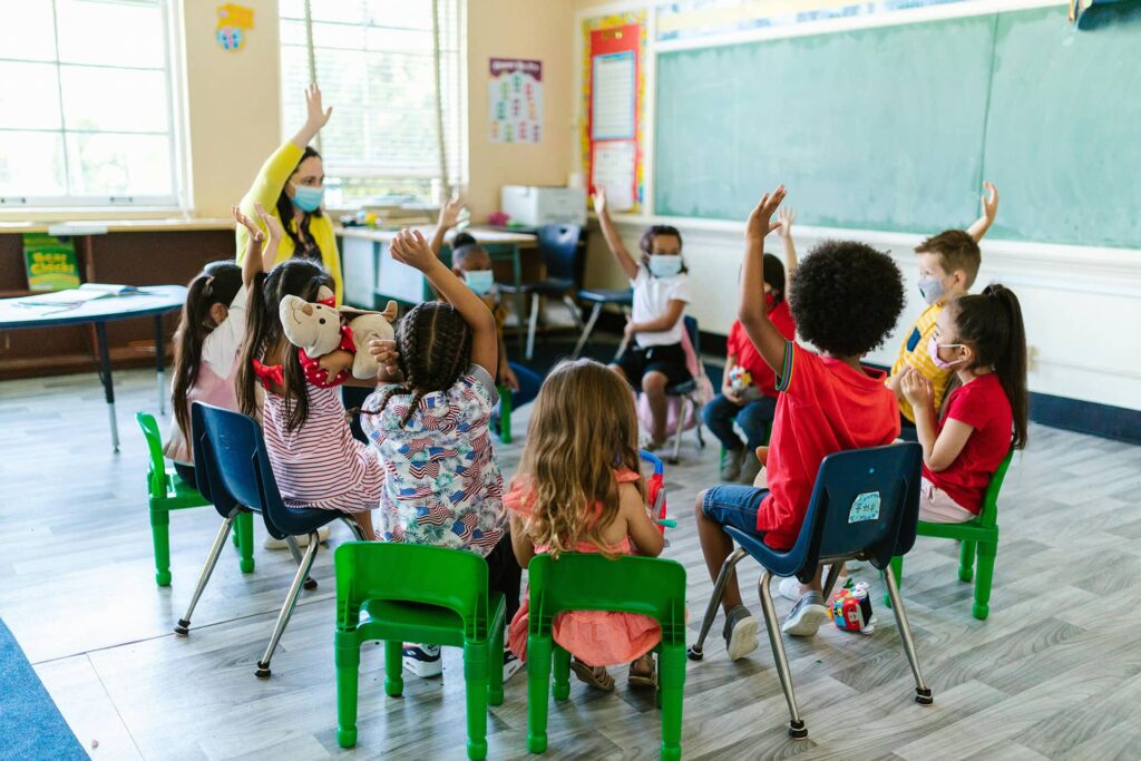 Group of students raising their hands while sitting in circle in classroom