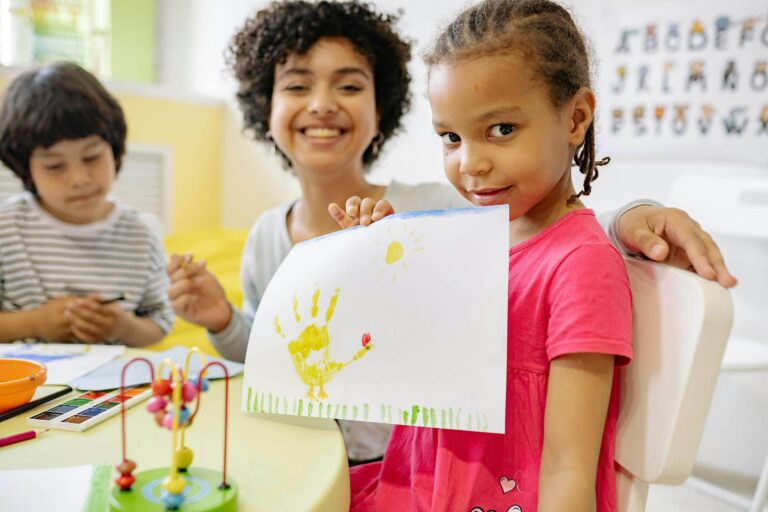 Young student smiling at camera holding up a hand painting.