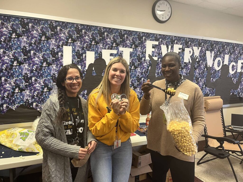 Three women smiling at camera holding popcorn and peace symbol stickers