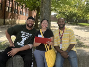 Three adults sitting on bench near a tree