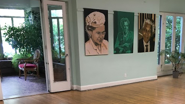 Room with paintings on wall and view of nature outside.